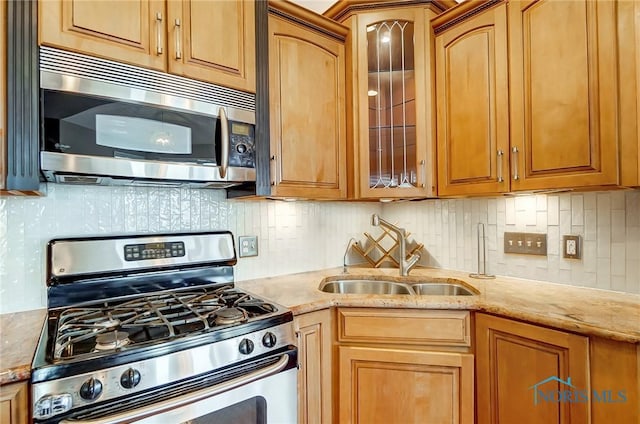 kitchen with appliances with stainless steel finishes, sink, light stone counters, and decorative backsplash