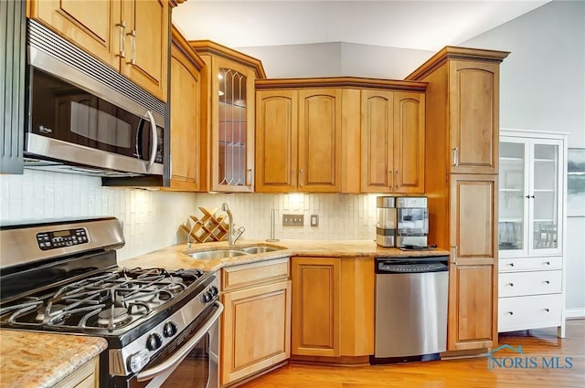 kitchen featuring sink, light stone counters, light wood-type flooring, stainless steel appliances, and backsplash