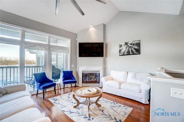 living room with hardwood / wood-style floors, a high end fireplace, ceiling fan, and vaulted ceiling