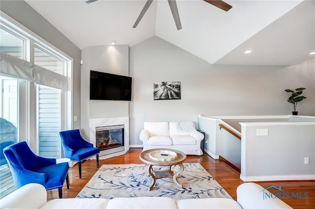 living room featuring dark wood-type flooring, ceiling fan, a premium fireplace, and vaulted ceiling