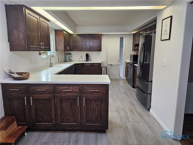 kitchen with refrigerator, sink, dark brown cabinetry, kitchen peninsula, and black / electric stove