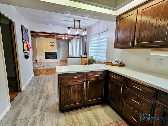 kitchen featuring pendant lighting, a brick fireplace, dark brown cabinets, and kitchen peninsula