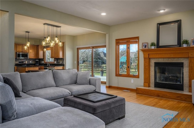 living room with a tiled fireplace, sink, and light hardwood / wood-style floors