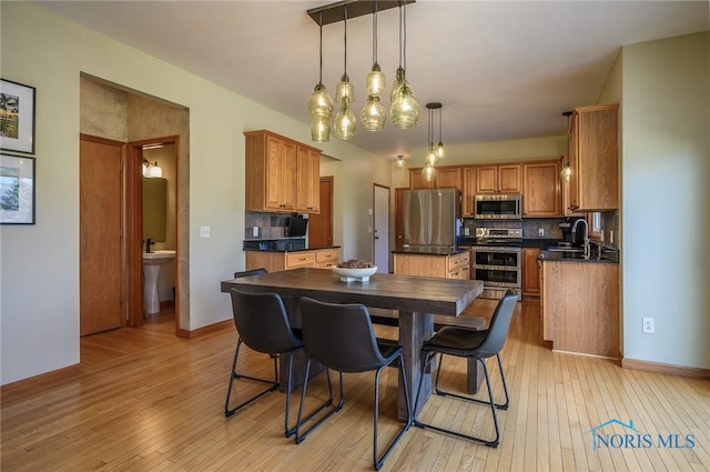 kitchen with appliances with stainless steel finishes, hanging light fixtures, a center island, light hardwood / wood-style floors, and decorative backsplash