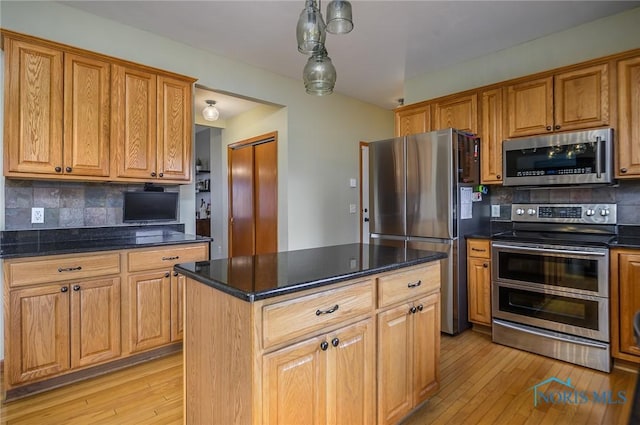 kitchen with decorative light fixtures, a center island, light wood-type flooring, appliances with stainless steel finishes, and decorative backsplash