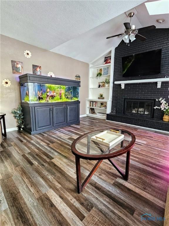 living room with lofted ceiling with skylight, a brick fireplace, a textured ceiling, and dark hardwood / wood-style flooring