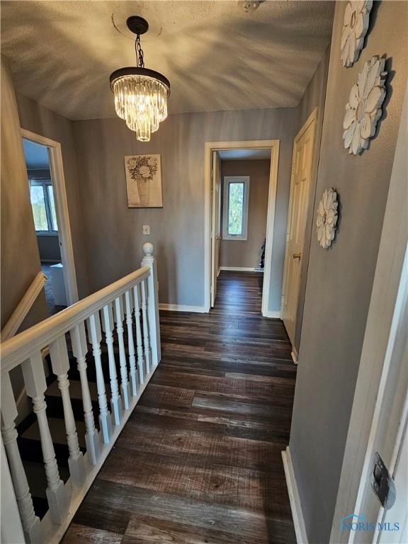 hallway featuring dark wood-type flooring, a chandelier, and a textured ceiling