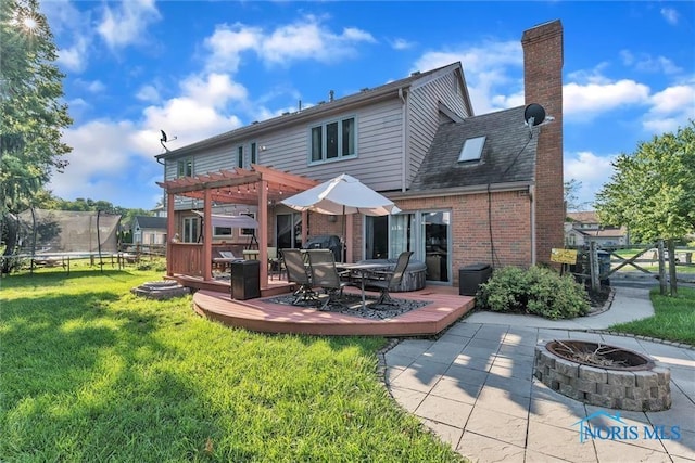 rear view of property with a wooden deck, a pergola, a fire pit, and a trampoline