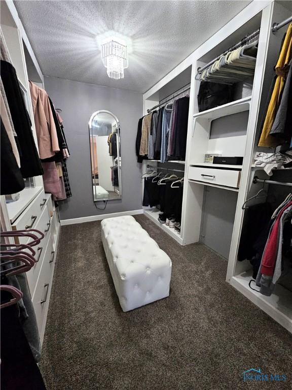 spacious closet featuring an inviting chandelier and dark carpet