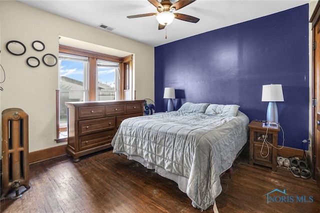 bedroom with dark wood-style floors, visible vents, radiator heating unit, ceiling fan, and baseboards