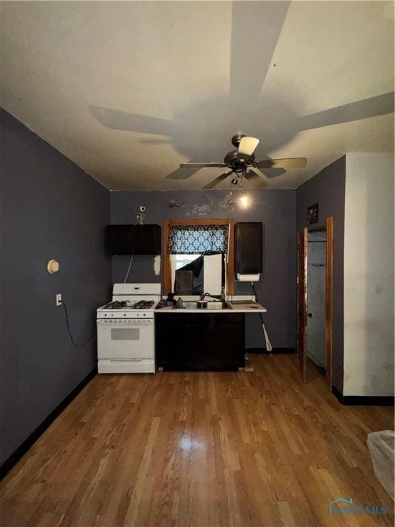 kitchen with wood finished floors, a sink, baseboards, and white gas range