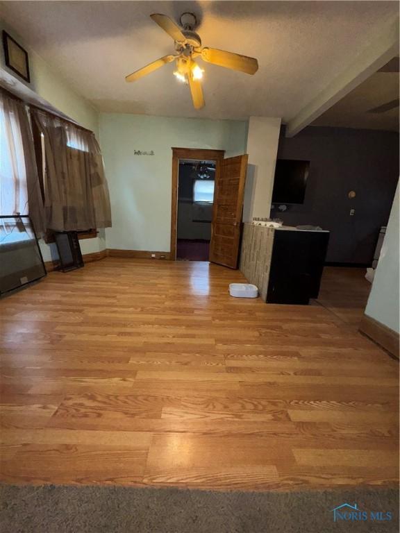 unfurnished living room with beam ceiling, light wood-style flooring, a healthy amount of sunlight, ceiling fan, and baseboards