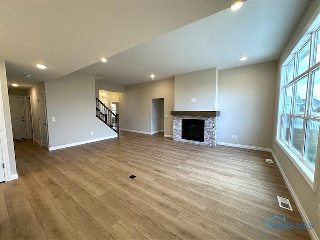 unfurnished living room with a stone fireplace and light wood-type flooring