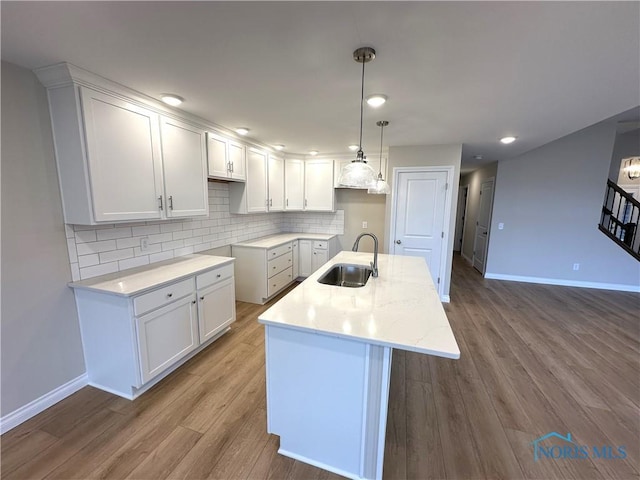 kitchen with hardwood / wood-style floors, white cabinetry, sink, backsplash, and a kitchen island with sink