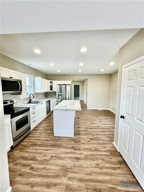 kitchen featuring appliances with stainless steel finishes, white cabinetry, light stone countertops, a kitchen island, and light wood-type flooring