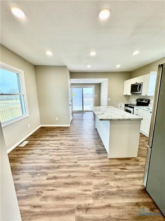 kitchen featuring appliances with stainless steel finishes, a center island, light stone countertops, light hardwood / wood-style floors, and white cabinets