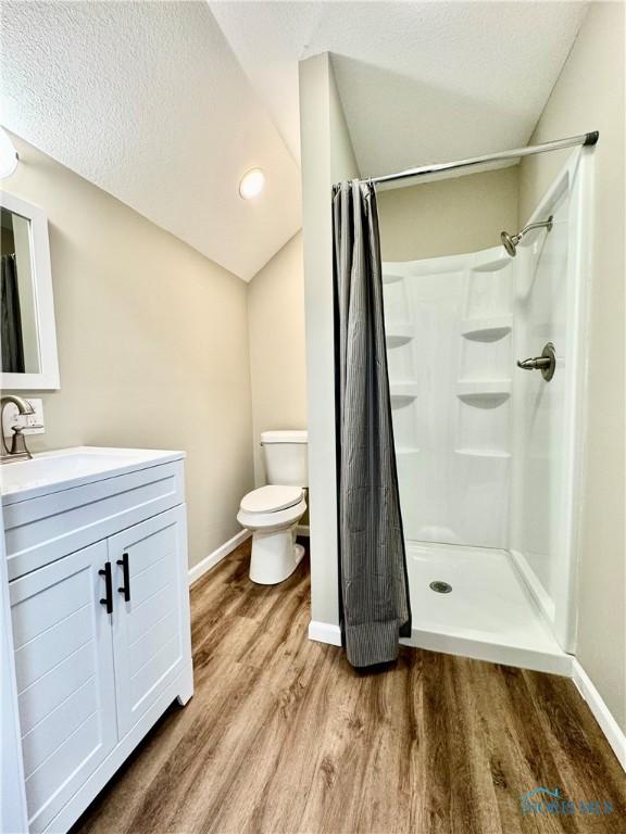 bathroom with hardwood / wood-style floors, vanity, walk in shower, toilet, and a textured ceiling