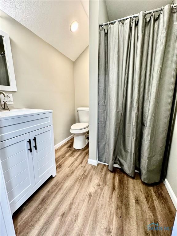 bathroom featuring vanity, vaulted ceiling, hardwood / wood-style floors, and toilet