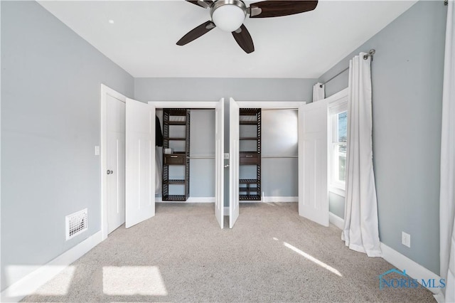 unfurnished bedroom featuring light carpet, two closets, and ceiling fan