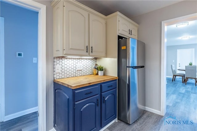 kitchen featuring butcher block countertops, decorative backsplash, stainless steel refrigerator, and white cabinets