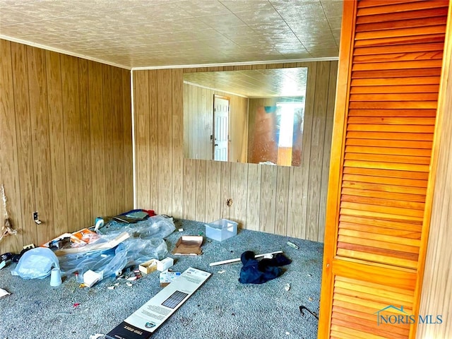 unfurnished bedroom featuring carpet floors, wooden walls, and ornamental molding