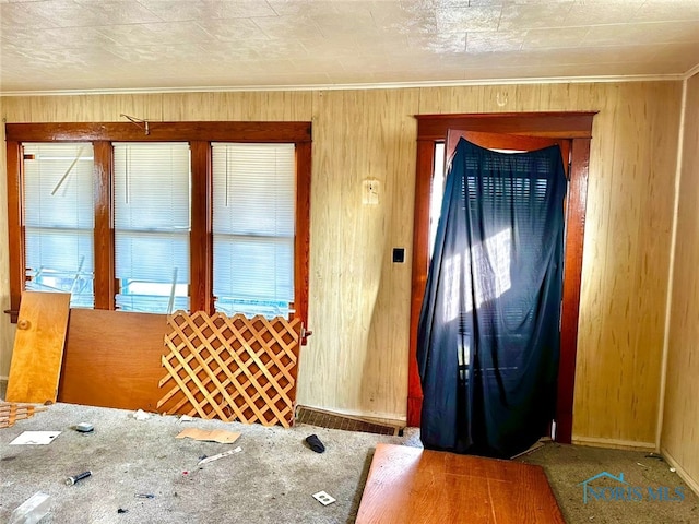 doorway to outside with carpet, ornamental molding, and wood walls