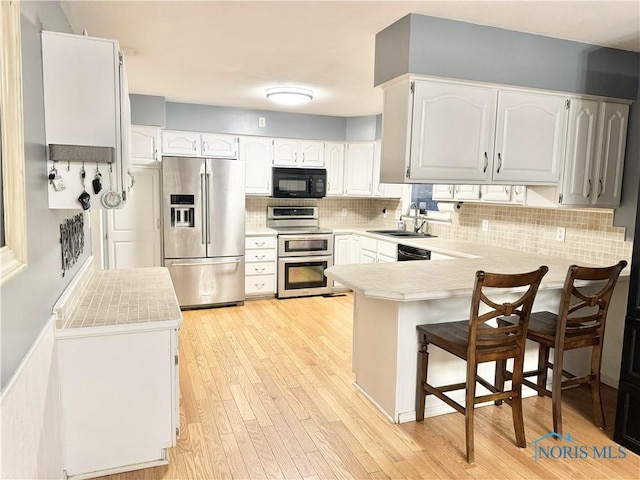 kitchen featuring sink, black appliances, kitchen peninsula, decorative backsplash, and white cabinets