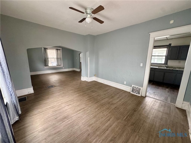 unfurnished living room with a wealth of natural light, dark wood-type flooring, and ceiling fan