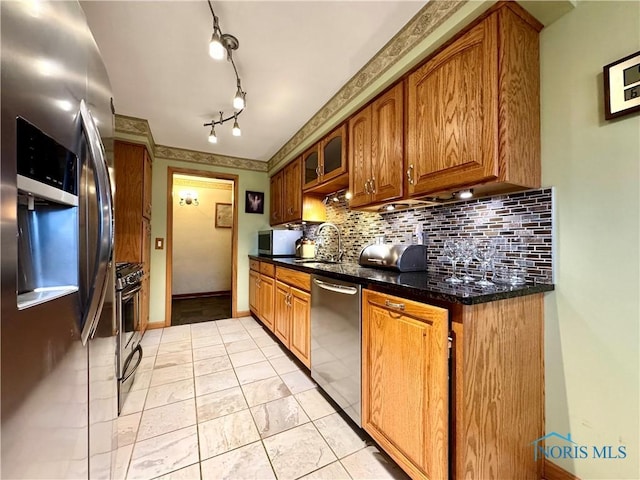 kitchen with tasteful backsplash, appliances with stainless steel finishes, sink, and dark stone countertops