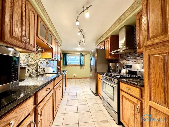 kitchen with light tile patterned flooring, sink, dark stone countertops, stainless steel appliances, and wall chimney range hood