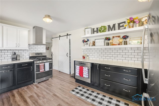 kitchen featuring white cabinetry, exhaust hood, light hardwood / wood-style floors, stainless steel appliances, and a barn door