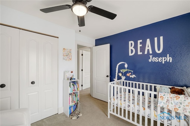 carpeted bedroom with a nursery area, ceiling fan, and a closet