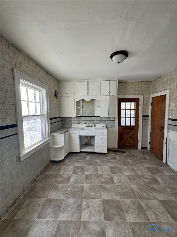 kitchen featuring a healthy amount of sunlight, sink, tile walls, and white cabinets