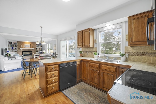 kitchen featuring sink, decorative light fixtures, light wood-type flooring, black dishwasher, and kitchen peninsula