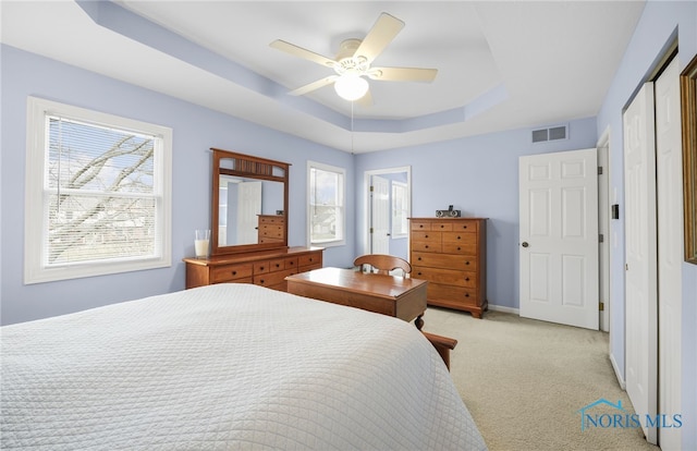 carpeted bedroom with a tray ceiling, a closet, and ceiling fan