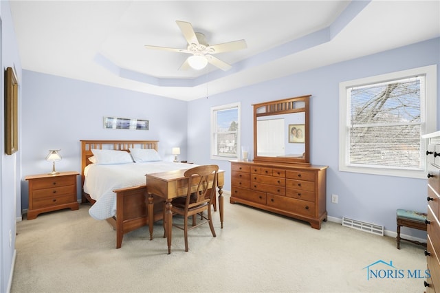 bedroom featuring ceiling fan, light colored carpet, and a tray ceiling