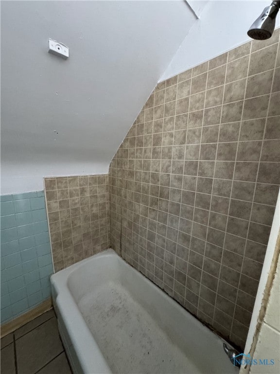 bathroom with lofted ceiling, a tub to relax in, tile patterned flooring, and tile walls