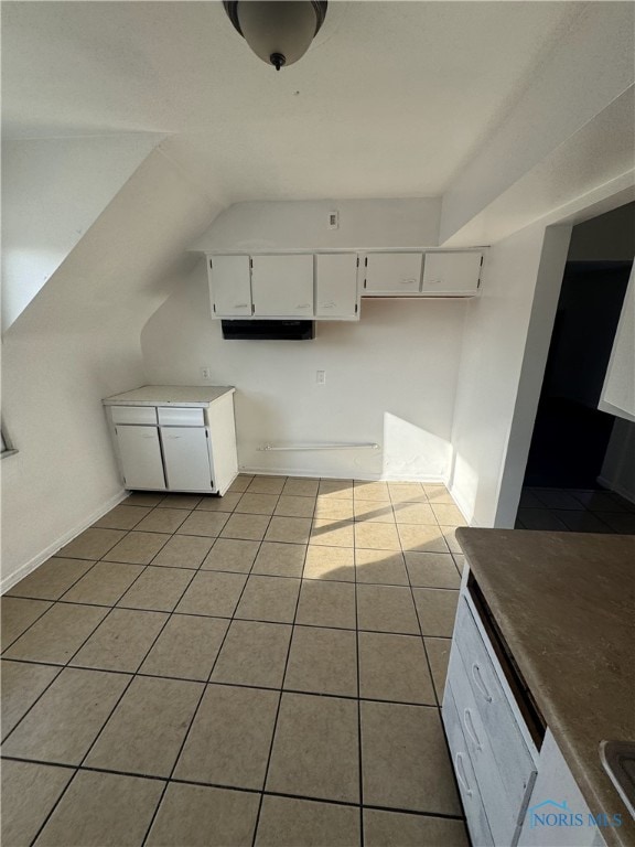 kitchen with white cabinetry, vaulted ceiling, and light tile patterned floors