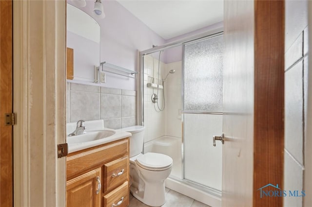 bathroom with a shower with door, tile walls, vanity, tile patterned floors, and toilet