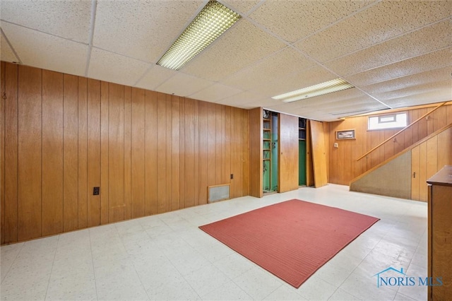 basement featuring wooden walls and a drop ceiling