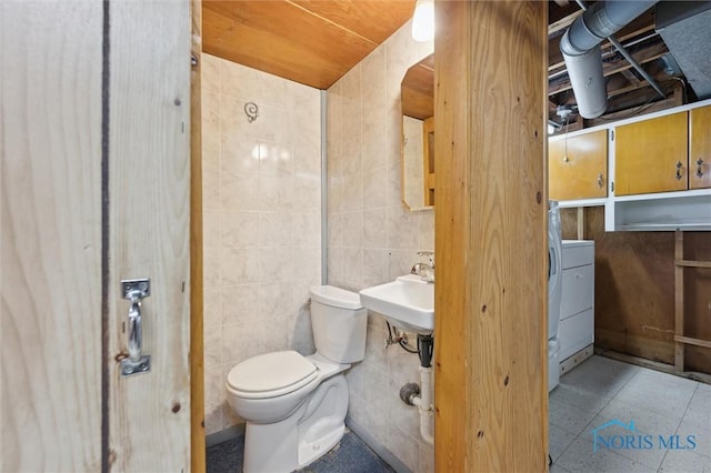 bathroom with washer / dryer, sink, tile walls, and toilet