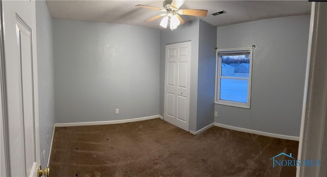 unfurnished bedroom with a ceiling fan, dark colored carpet, visible vents, and baseboards