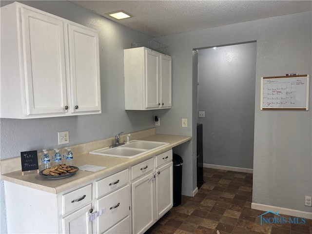 kitchen with a textured ceiling, light countertops, a sink, and white cabinets