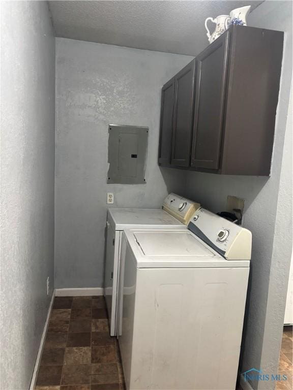 washroom featuring cabinet space, electric panel, baseboards, stone finish floor, and washing machine and dryer