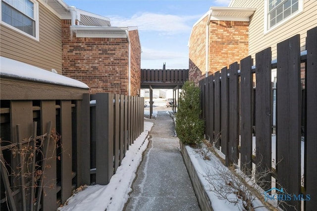 view of snowy exterior with brick siding and fence