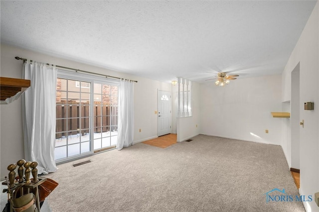 interior space featuring light carpet, baseboards, visible vents, ceiling fan, and a textured ceiling