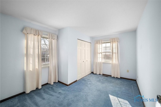 unfurnished bedroom featuring carpet floors, multiple windows, a closet, and baseboards