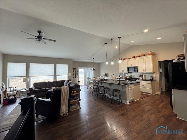 kitchen featuring a breakfast bar, dark hardwood / wood-style floors, white cabinetry, black appliances, and a center island with sink