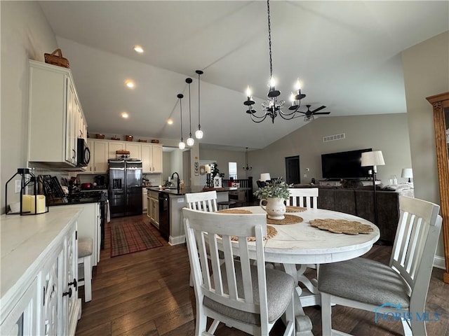 dining area with dark hardwood / wood-style flooring, sink, vaulted ceiling, and an inviting chandelier