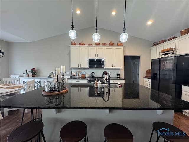 kitchen with appliances with stainless steel finishes, vaulted ceiling, white cabinetry, hanging light fixtures, and a kitchen island with sink